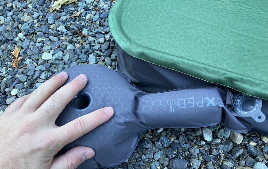 Hand using the mini hand pump to inflate the Exped MegaMat 10 sleeping pad.